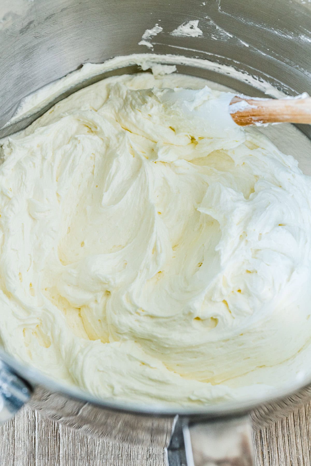 Vanilla buttercream frosting in a mixing bowl with wooden spatula