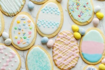 Easter Sugar Cookies with pastel colors, sprinkles and egg-shaped candies on marble countertop