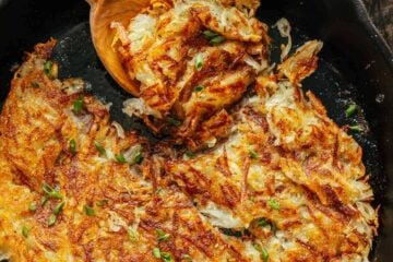 Hash browns in a cast iron skillet with a serving spoon