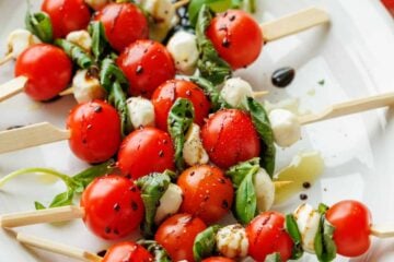 Caprese skewers recipe with tomatoes, basil, mozzarella pearls and balsamic glaze on a white plate