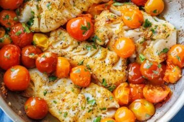 Flakey sauteed cod in a skillet with tomatoes and parsley garnish.