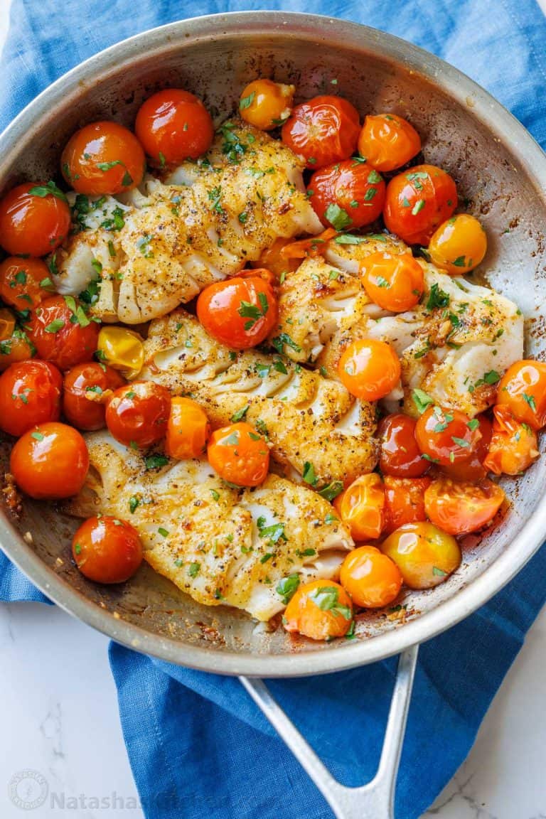 Flakey sauteed cod in a skillet with tomatoes and parsley garnish.