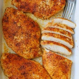 baked chicken breast sliced and served in a white casserole dish with a fork