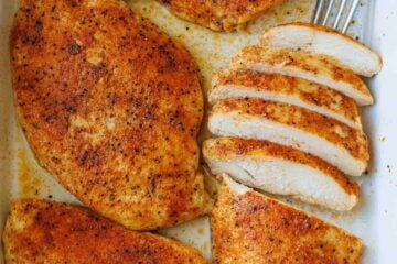 baked chicken breast sliced and served in a white casserole dish with a fork