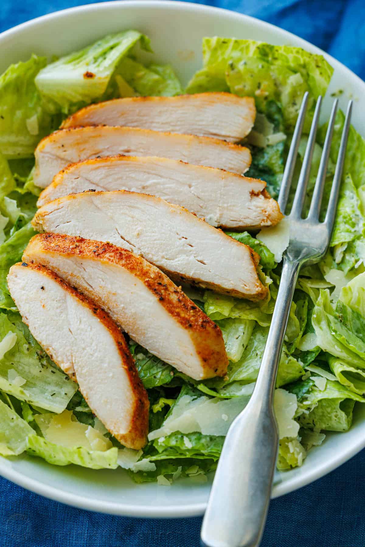 Sliced baked chicken breast served over green salad