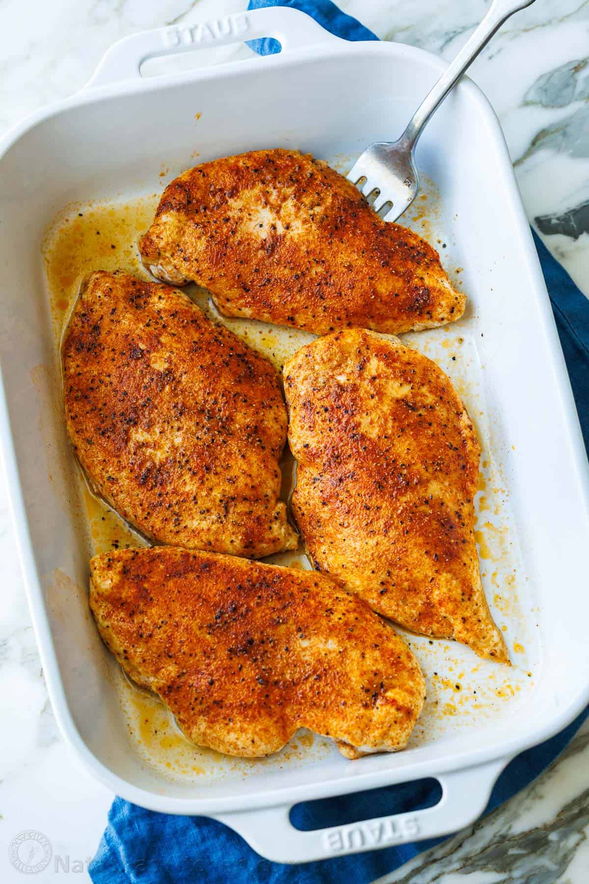 Baked chicken Breasts in white casserole dish with serving fork