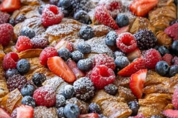 Dusting powdered sugar over croissant French Toast Casserole in a white dish
