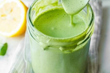 Homemade Green Goddess Dressing in a mason job and dripping from a spoon