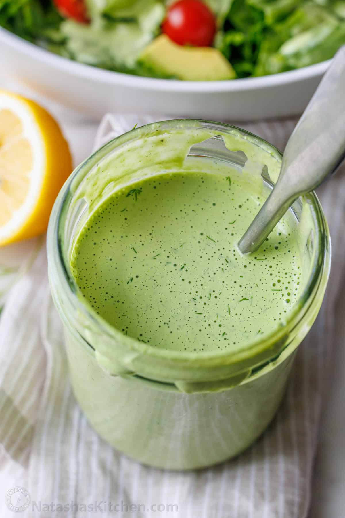 Homemade Green Goddess Dressing is easy to make and tastes so fresh and vibrant. It takes just 30 seconds from blender to topping salads! Green Goddess Salad Dressing in a mason jar mixed with a spoon and dotted with tiny specs of dill.
