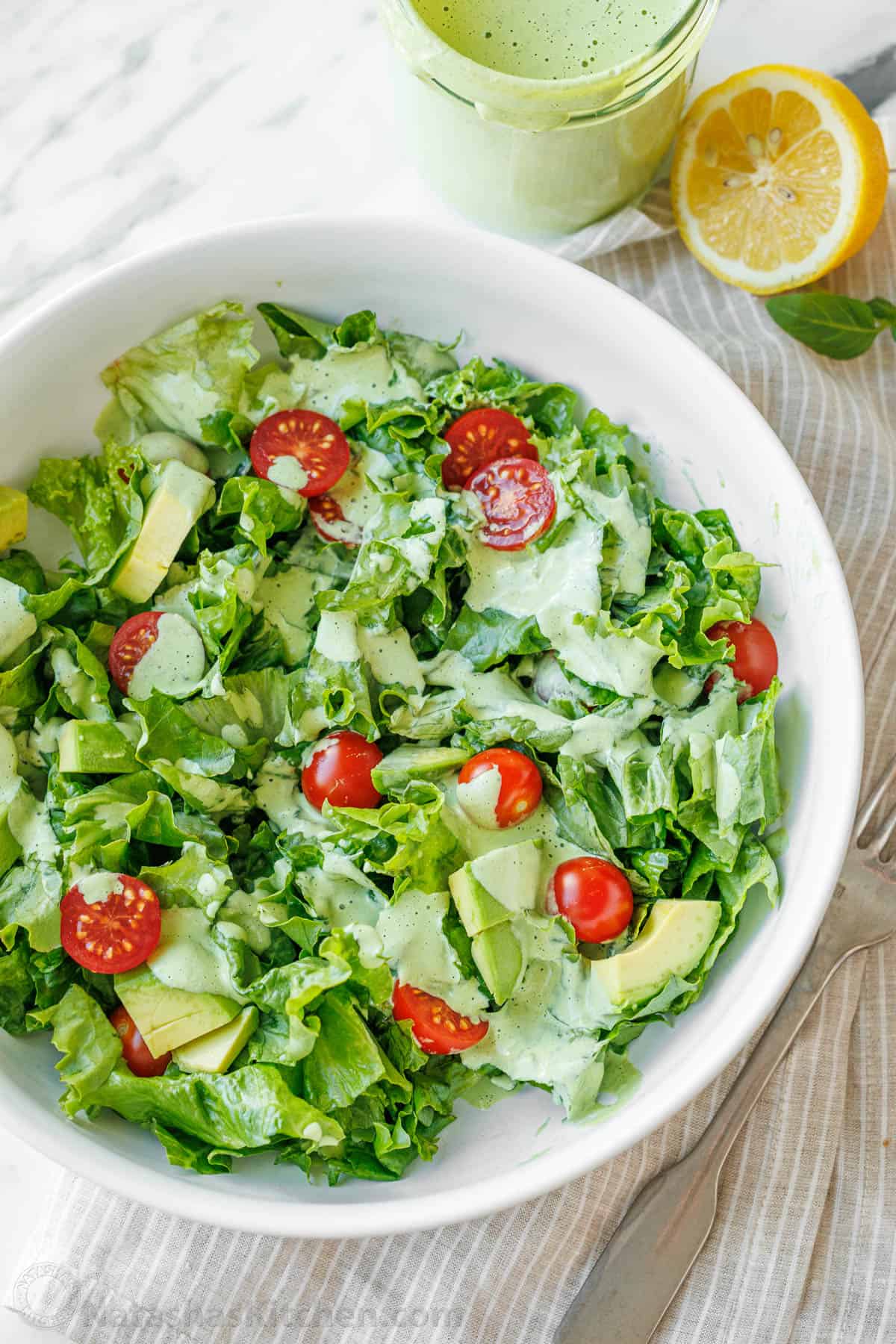 Homemade Green Goddess Dressing is easy to make and tastes so fresh and vibrant. It takes just 30 seconds from blender to topping salads! Fresh salad with tomatoes covered with Greek Goddess Dressing in a white bowl