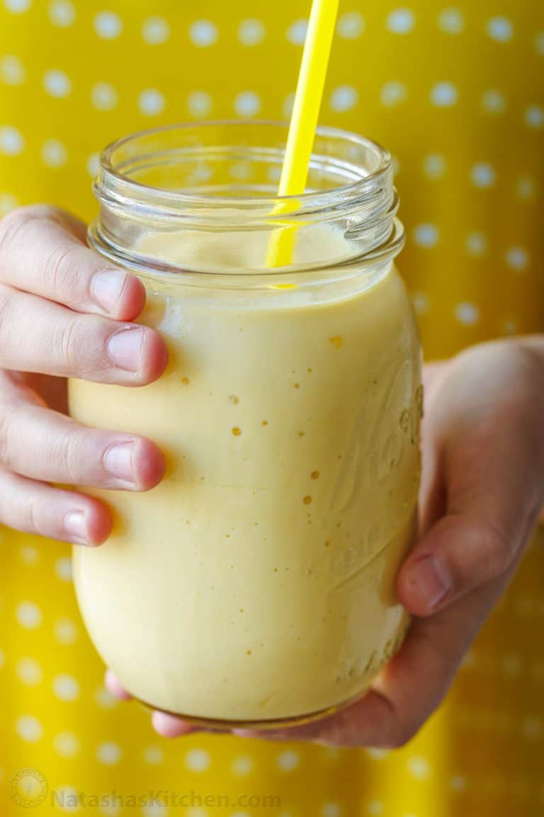 hands holding a yellow mango smoothie in a mason jar with yellow polka-dot background