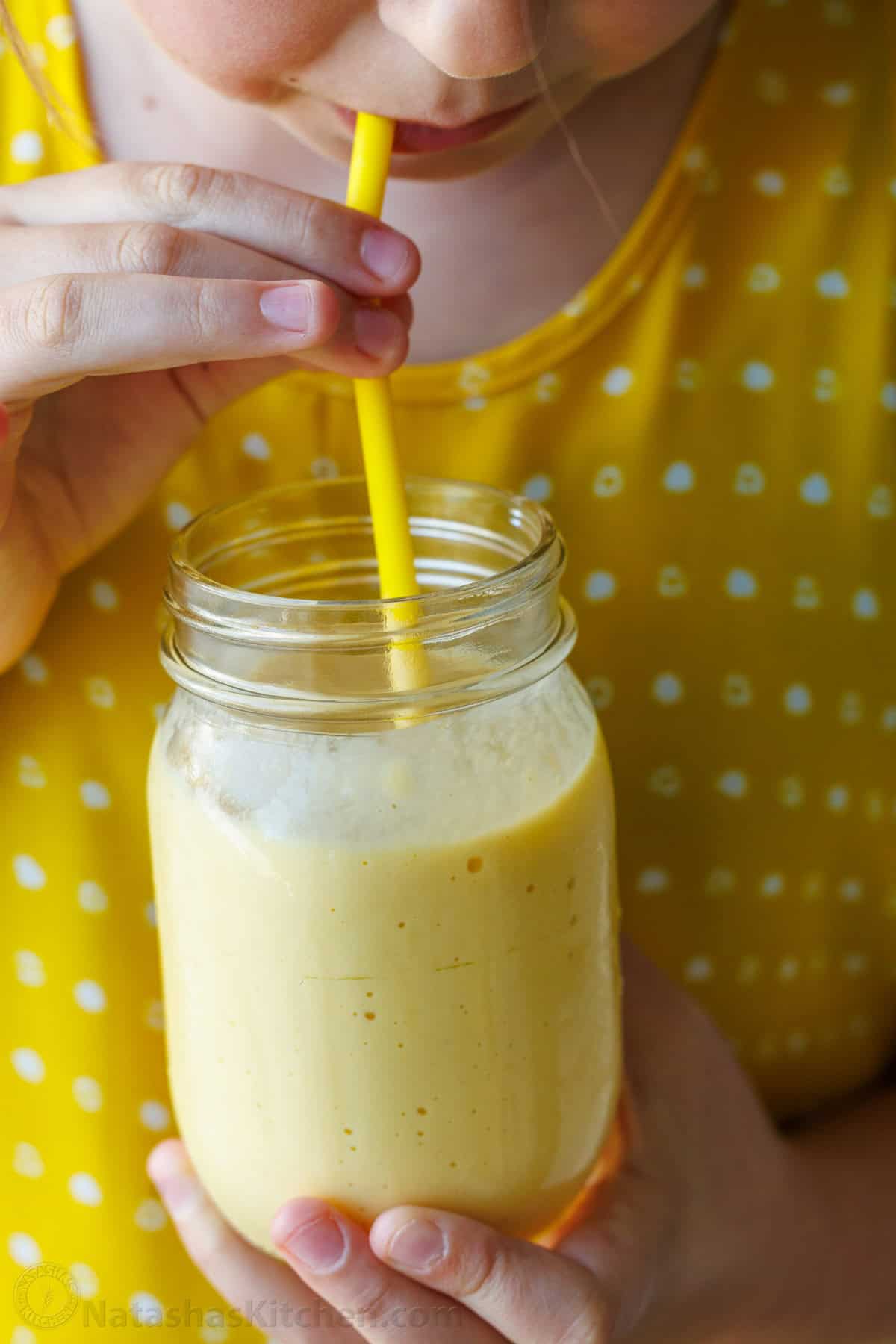 Small girl drinking a Mango smoothie in a mason jar with a yellow jar