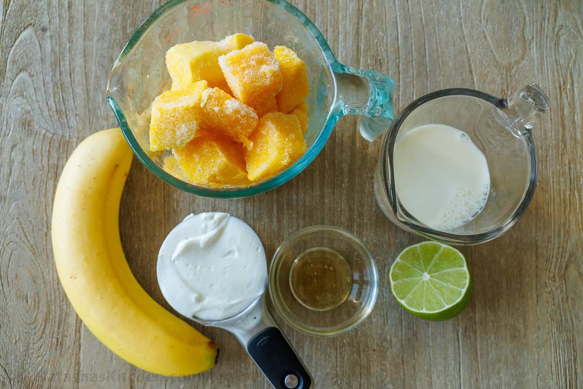 ingredients for tropical slushie with frozen fruit, banana, greek yogurt, honey, milk and lime