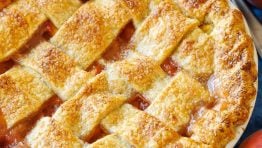 Peaches surrounding a homemade peach pie with browned crust and pie server