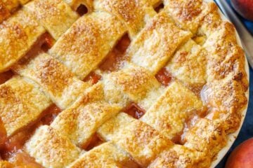 Peaches surrounding a homemade peach pie with browned crust and pie server