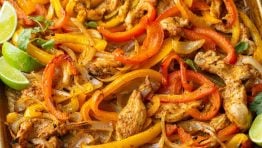 sheet pan chicken fajitas cooked on a cookie sheet with chicken, red and yellow peppers, onions and lime wedges