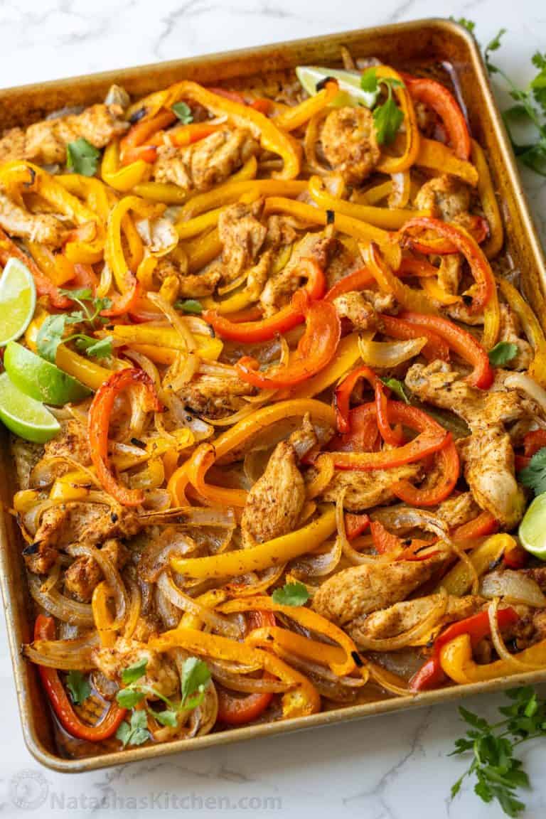 sheet pan chicken fajitas cooked on a cookie sheet with chicken, red and yellow peppers, onions and lime wedges