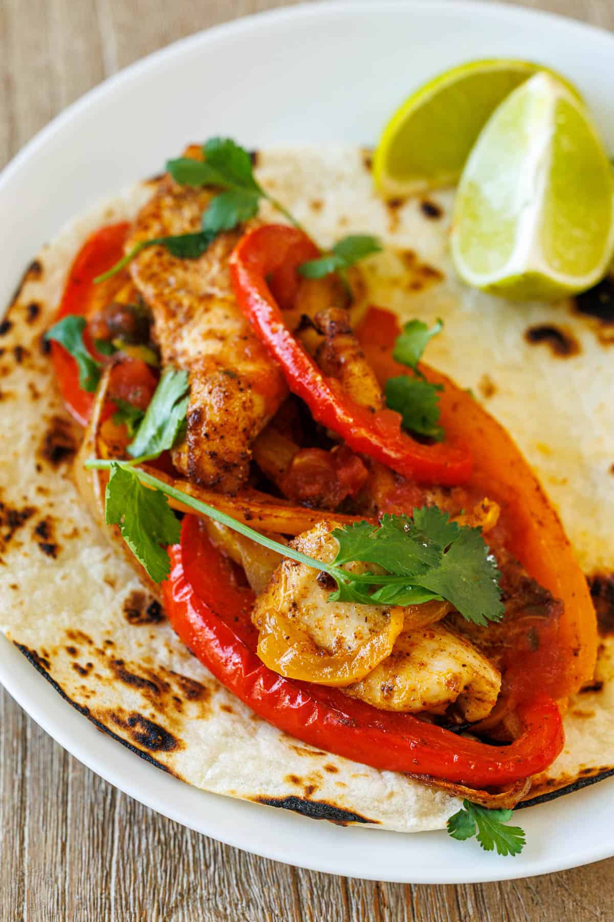 This Sheet Pan Chicken Fajitas recipe is packed with flavor. A crowd-pleasing, 30-minute, one-pan meal that makes any weeknight a fiesta! Mexican chicken fajita on a white plate with lime and cilantro to garnish