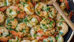 shrimp scampi recipe cooked in a sauté pan on the stove with a wooden spoon and garnished with parsley