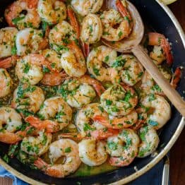 shrimp scampi recipe cooked in a sauté pan on the stove with a wooden spoon and garnished with parsley