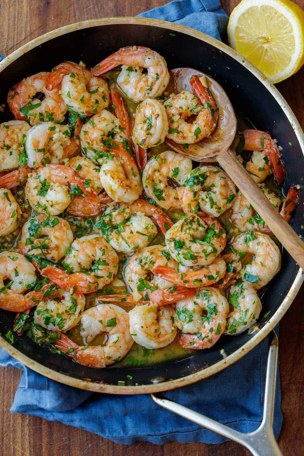 shrimp scampi recipe cooked in a sauté pan on the stove with a wooden spoon and garnished with parsley