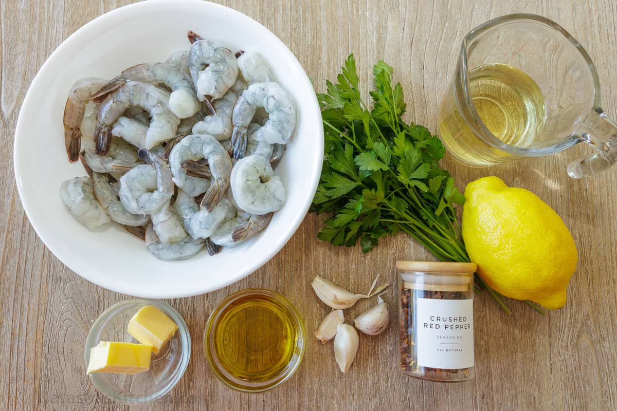 Ingredients for seafood appetizer including raw seafood, butter, oil, garlic, parsley, white wine, red pepper flakes and lemon