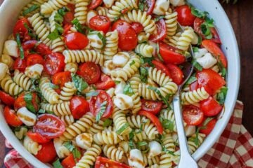 Caprese pasta salad recipe in a white bowl with a spoon for serving.