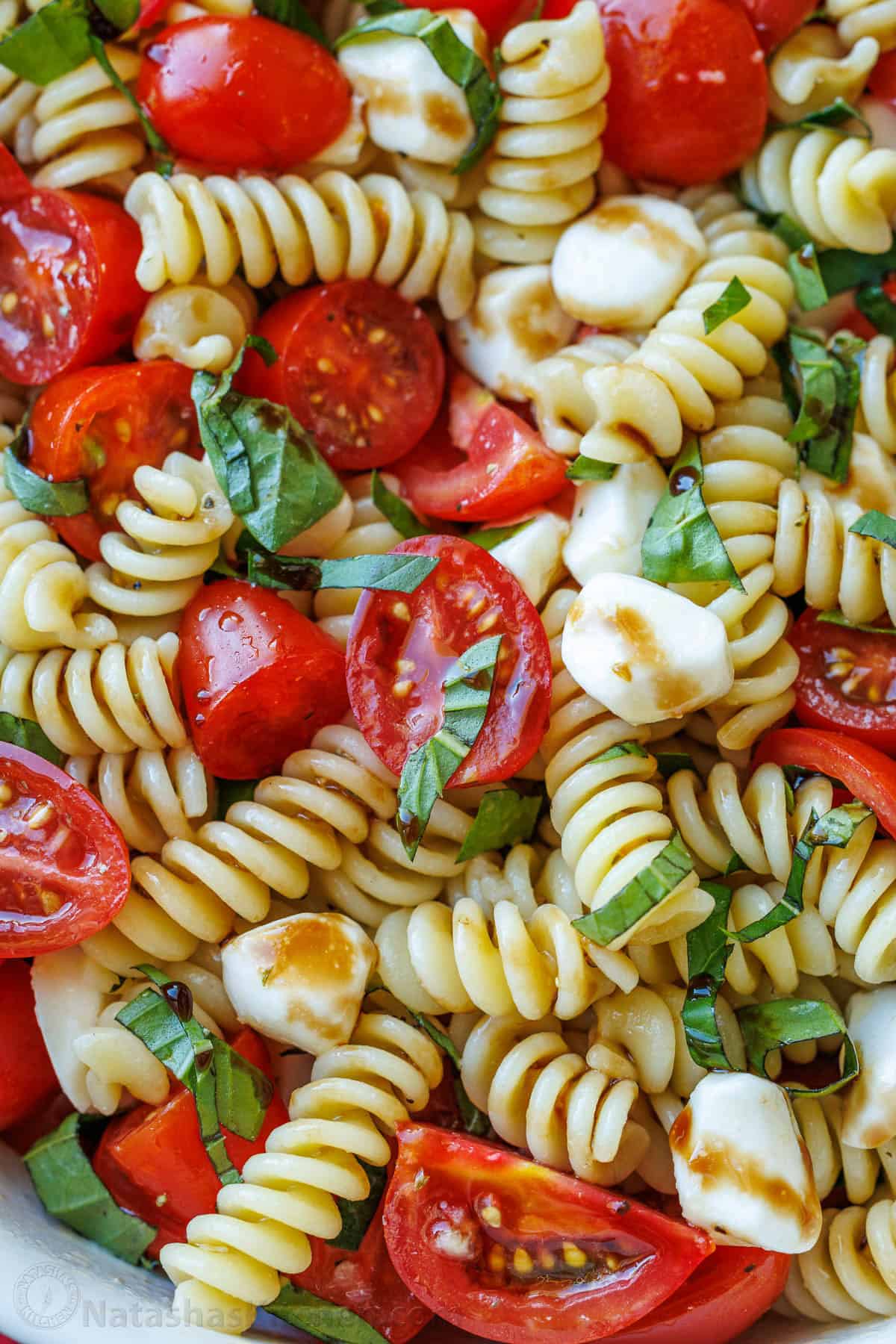 Caprese pasta salad combines the classic Caprese flavors of tomato, mozzarella and basil with Italian pasta salad. Perfect for BBQ potlucks. Caprese pasta salad with balsamic glaze and garnished with chopped basil