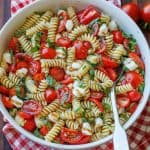 A bowl of Caprese Italian Pasta Salad in a white bowl with balsamic glaze and basil as garnish