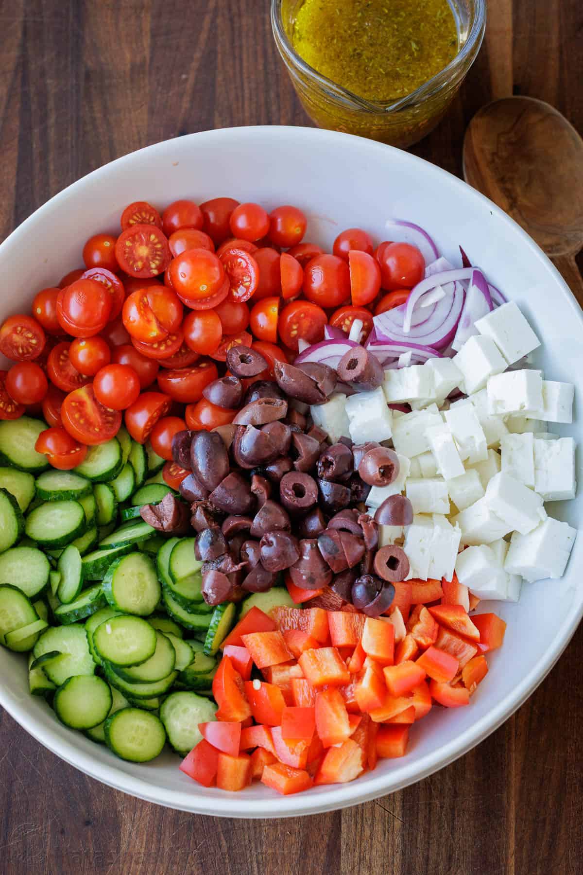 Vegetables sorted into a white bowl with dressing in a mason jar on the side