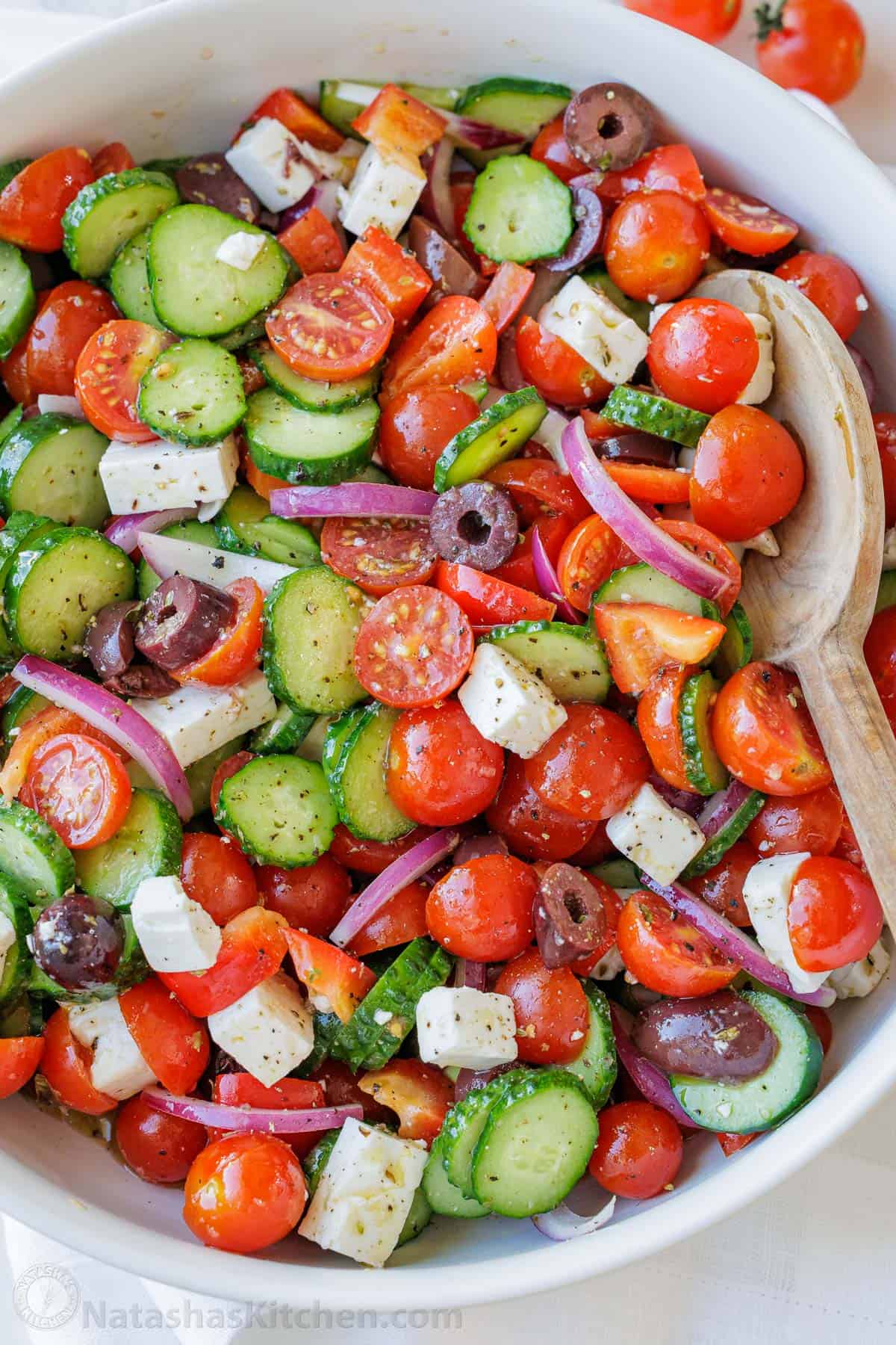 Greek Salad dressing covering tomatoes, cucumbers, feta cheese, red onions and olives