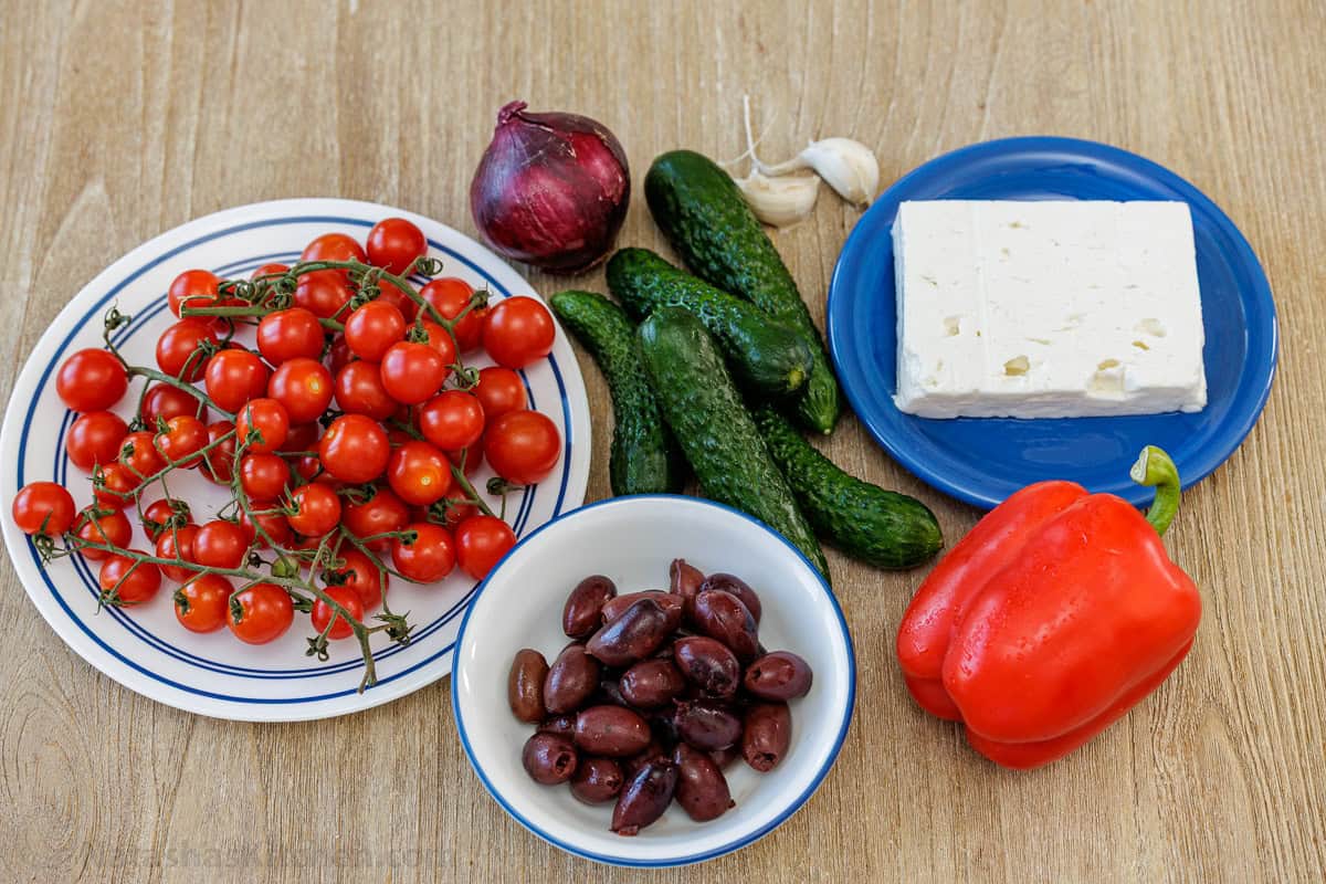 ingredients for classic side dish in Greece including cherry tomatoes, olives, cucumbers, red onion, garlic, feta and red bell pepper