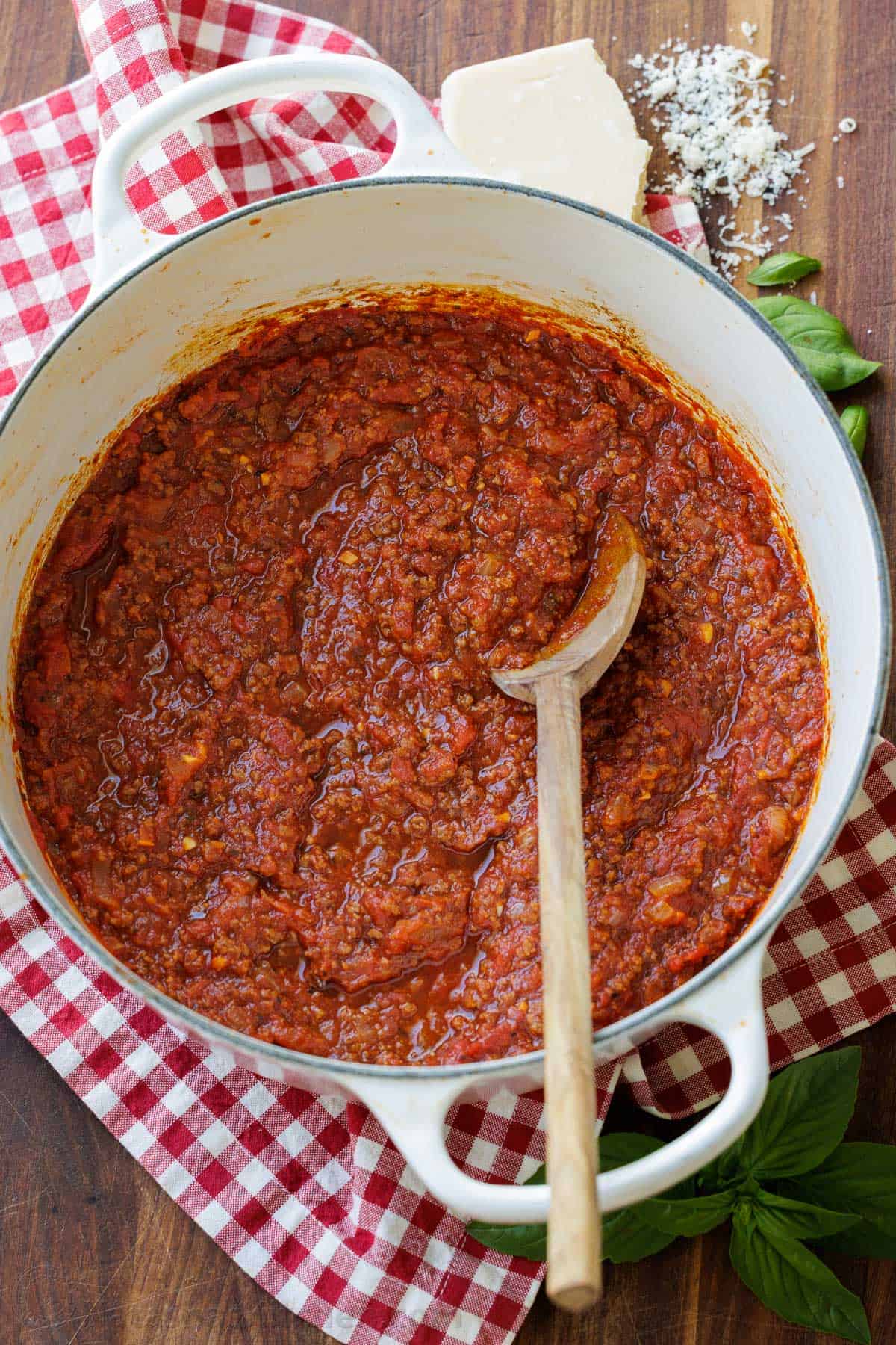 A wooden spoon stirring the Italian ground beef gravy in a Dutch oven