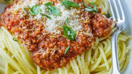 Spaghetti sauce recipe in a white bowl garnished with basil and parmesan cheese.