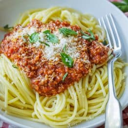 Spaghetti sauce recipe in a white bowl garnished with basil and parmesan cheese.