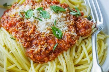 Spaghetti sauce recipe in a white bowl garnished with basil and parmesan cheese.