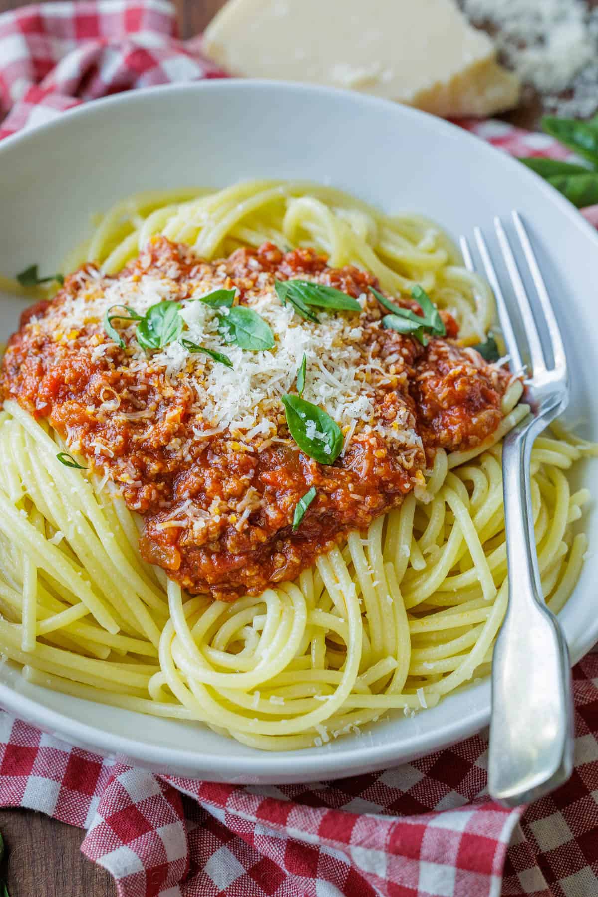 Spaghetti sauce recipe in a white bowl garnished with basil and parmesan cheese.