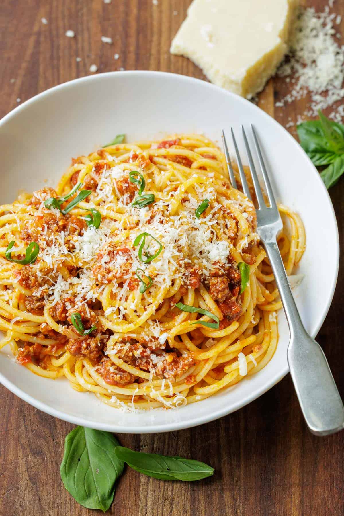 Spaghetti with meat sauce in a white bowl with basil and parmesan cheese garnish