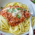 Spaghetti sauce spooned over pasta noodles in a white dish with a fork