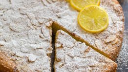 Almond cake with lemons and powdered sugar garnish on a dark tabletop