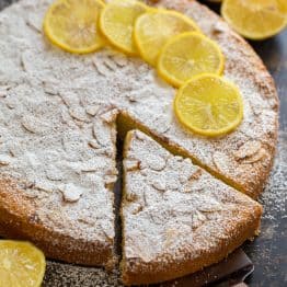 Almond cake with lemons and powdered sugar garnish on a dark tabletop
