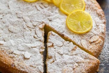 Almond cake with lemons and powdered sugar garnish on a dark tabletop