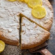 A slice of almond cake removed from the whole with almond slices and confectioners sugar on top