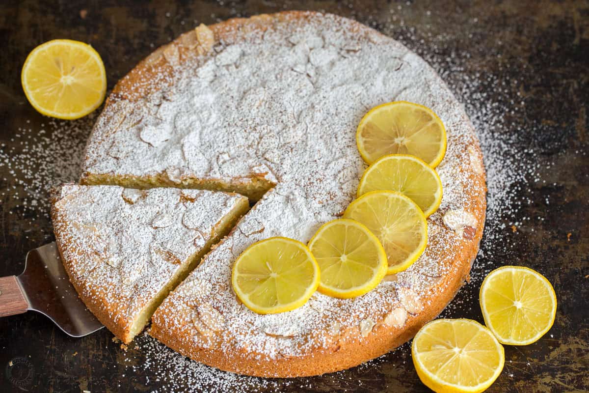 Almond cake recipe with slice cut and lemons and confectioners sugar on top