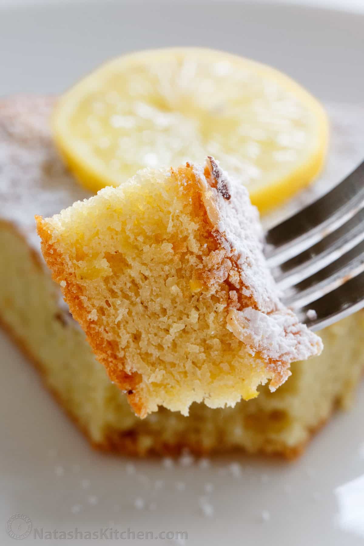 A bite of almond cake on a fork with powdered sugar dusted on top.