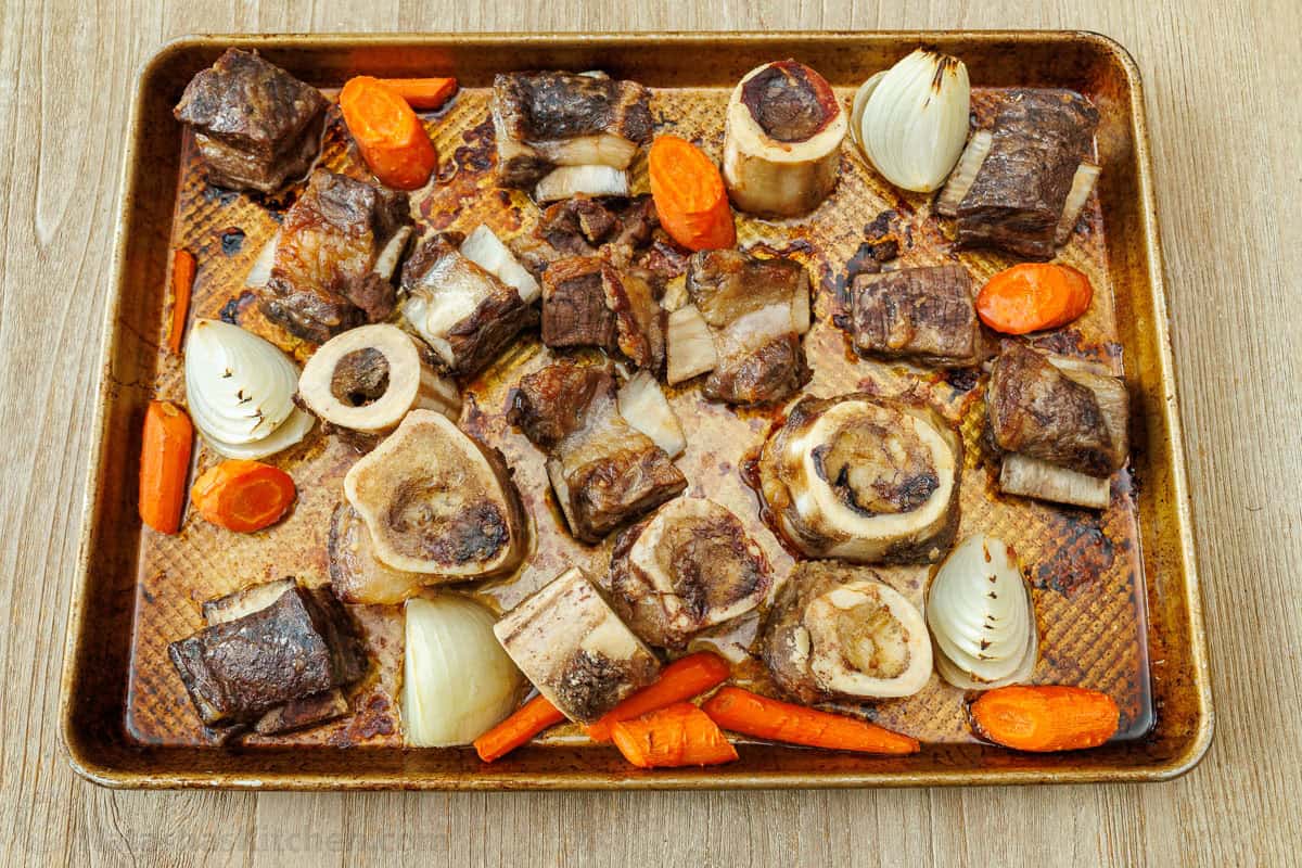 Make this easy beef stock in the slow cooker, stovetop, or Instant Pot. This beef bone broth is rich in flavor and better than store-bought. Roasted beef bones, meat and vegetables on a pan