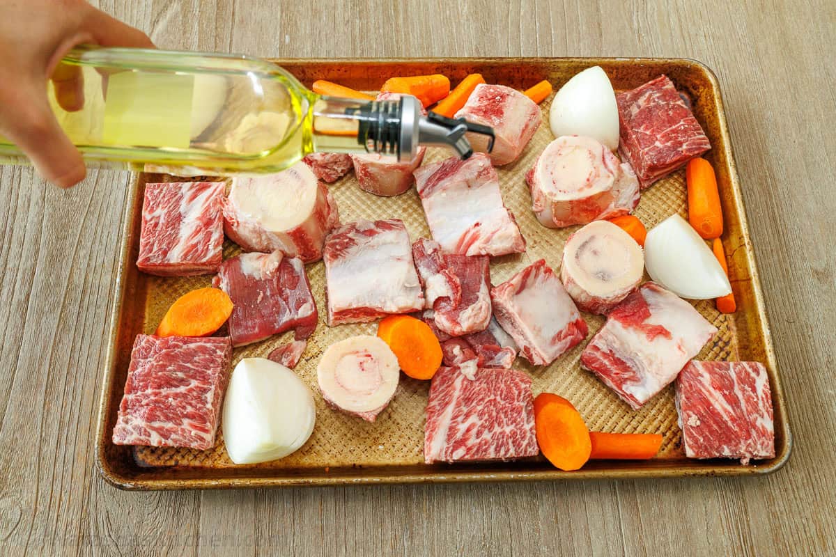 Make this easy beef stock in the slow cooker, stovetop, or Instant Pot. This beef bone broth is rich in flavor and better than store-bought. beef bones and vegetables on a roasting pan drizzling with olive oil
