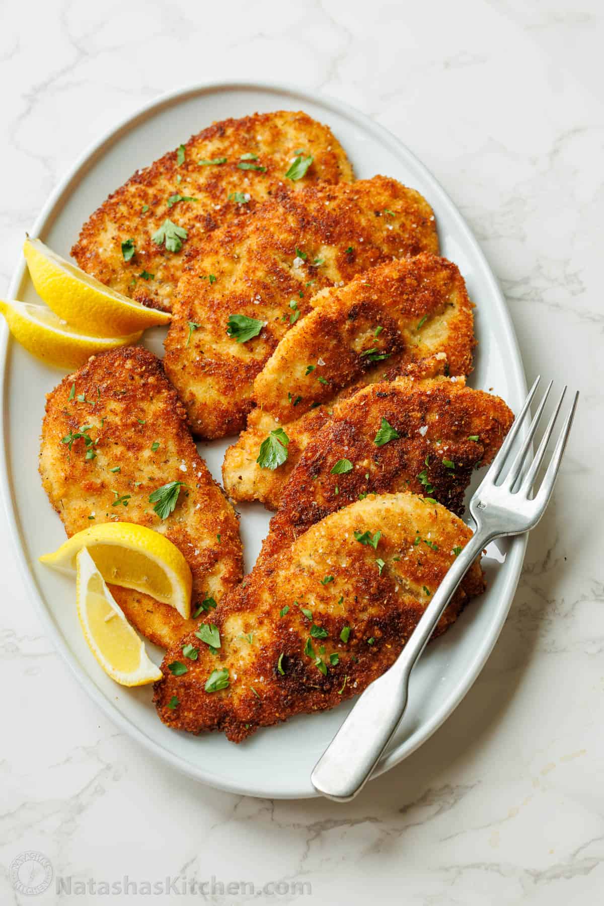 Easy breaded chicken cutlets recipe ready in under 30 minutes. Crispy on the outside with juicy chicken inside. Kid-friendly chicken dinner! Breaded Italian chicken cutlets on a white plate with a fork and lemon slices
