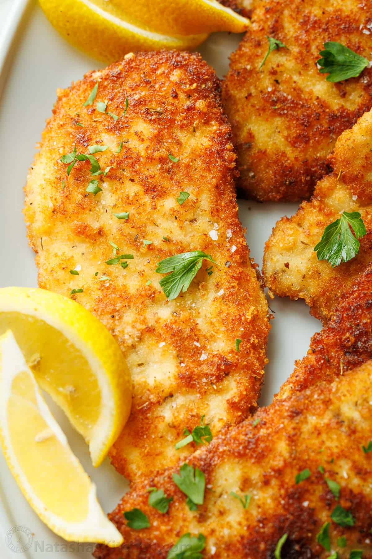 Easy breaded chicken cutlets recipe ready in under 30 minutes. Crispy on the outside with juicy chicken inside. Kid-friendly chicken dinner! Chicken Cutlets recipe on a plate with lemon slices and parsley garnish