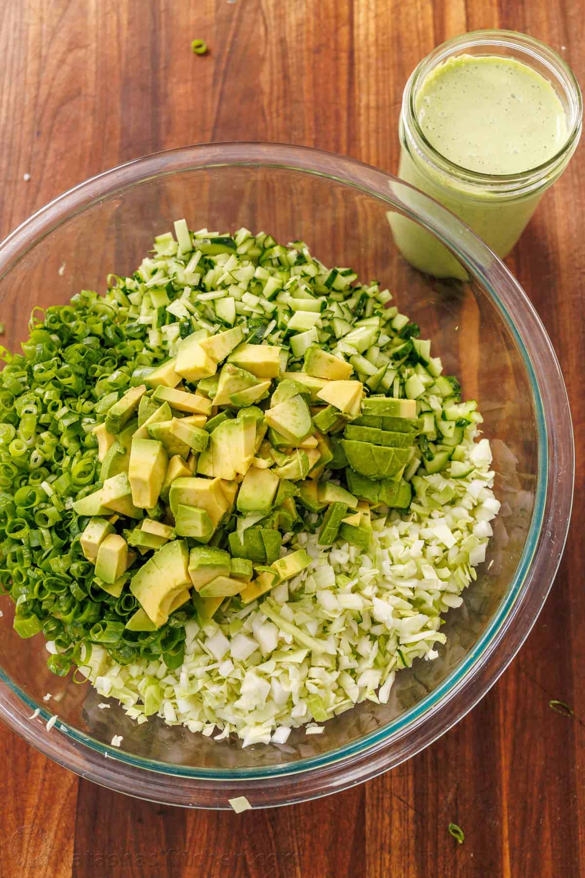 This easy Green Goddess Salad recipe comes together in minutes for the perfect side dish or lunch. Eat with a tortilla chip for a fun twist! Green Goddess Salad in a bowl with chopped cabbage, cucumbers, avocado, and green onion with Green Goddess dressing in a mason jar on the side